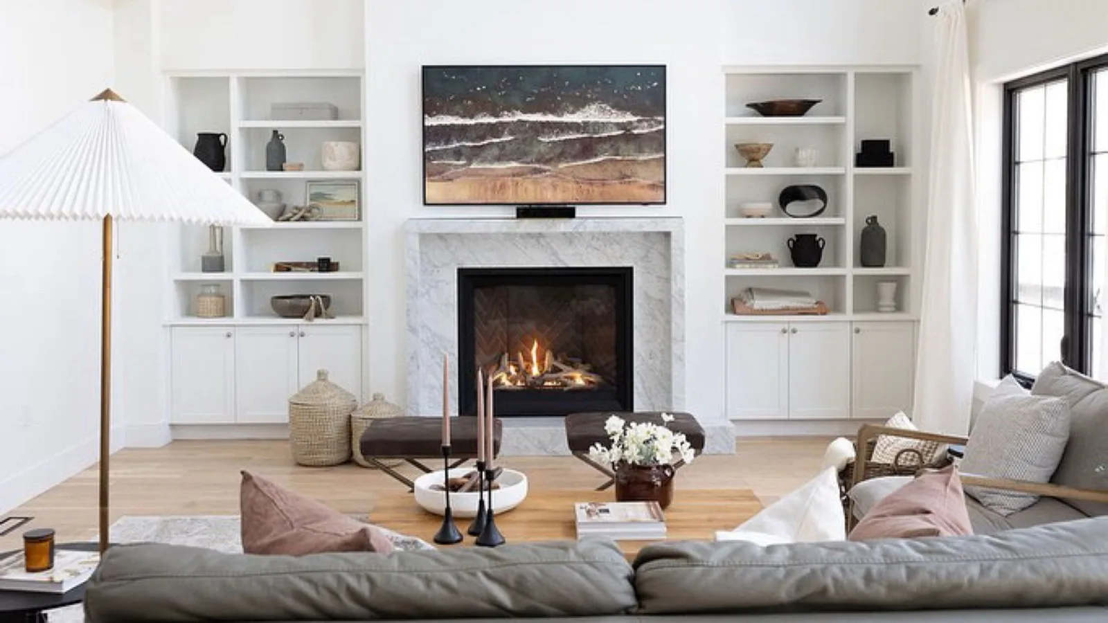 A linear gas fireplace burning below built-in white shelving in a styled family living room