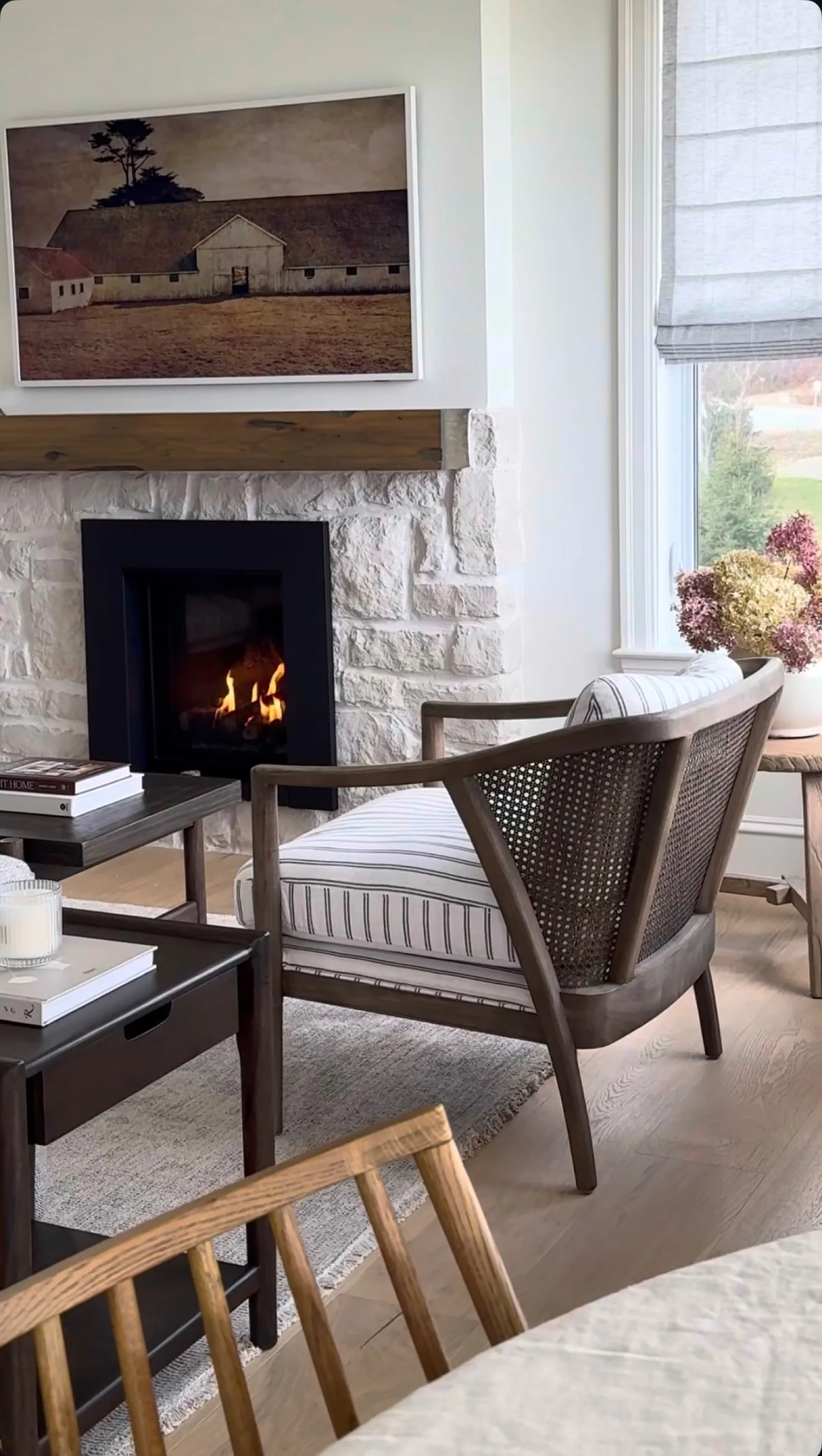 A gas stove burning inside a stone fireplace beside a woven chair