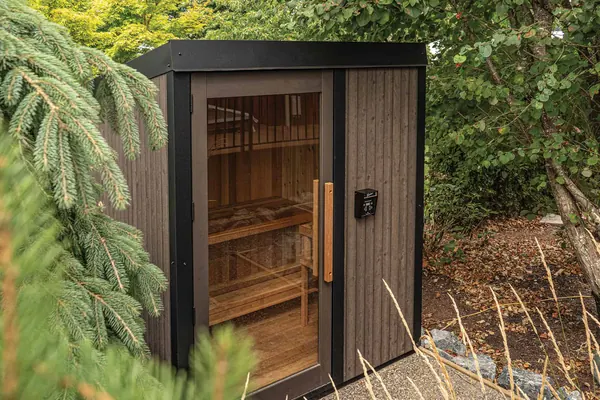 The Visscher Nature Series cedar sauna with its glass door, set among evergreens